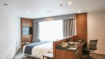 A hotel room with a bed, a desk, a chair, a TV, and a window with curtains.