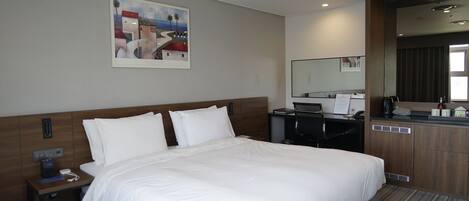 Habitación de hotel con una cama grande, un escritorio con silla, un espejo y un cuadro en la pared.