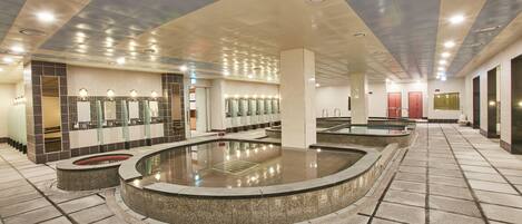 Un baño moderno con varios lavamanos, piscina climatizada central y suelo de baldosas.