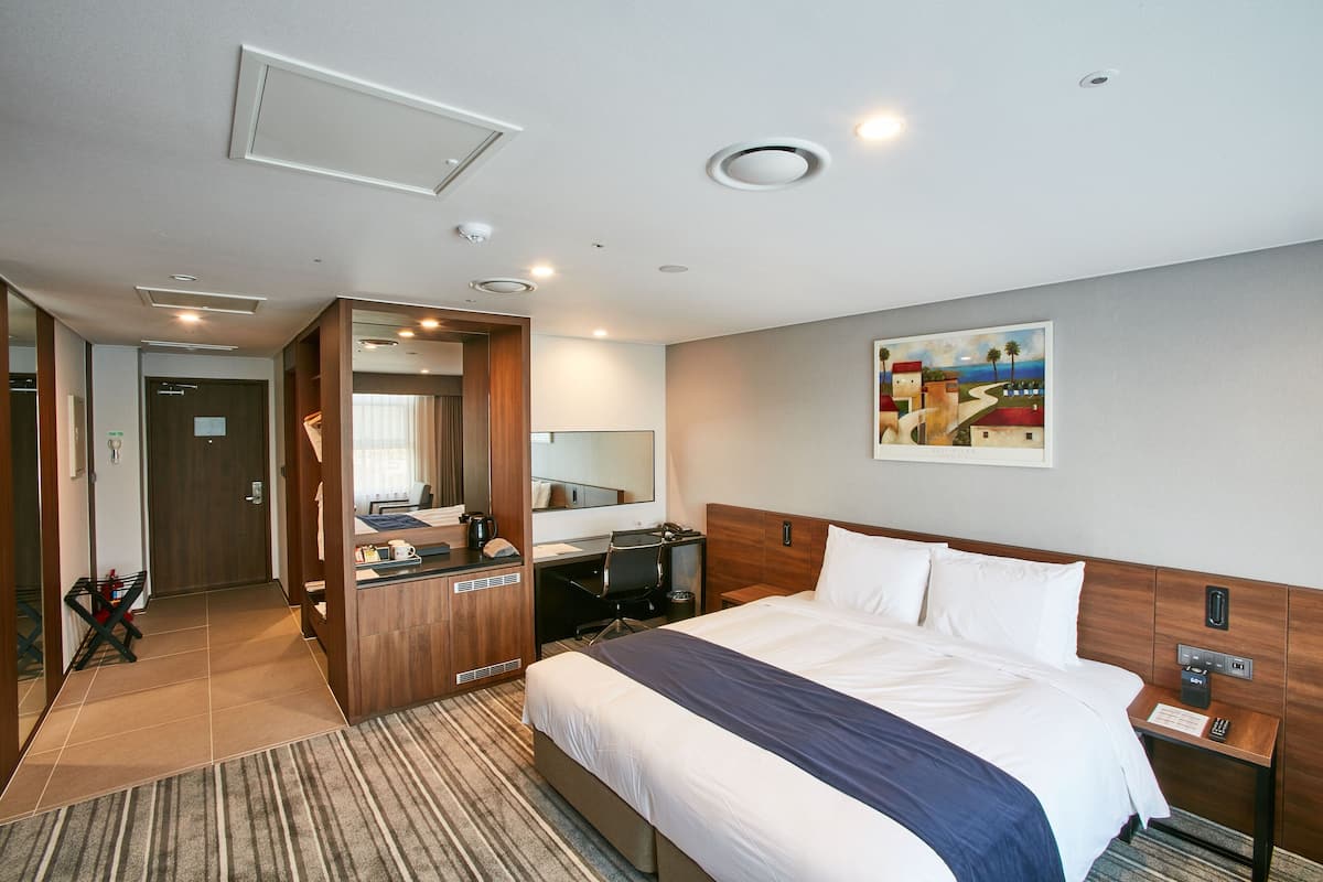 A hotel room with a large bed, a desk with a computer, a mirror, and a painting on the wall.