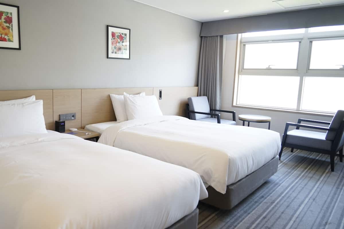 A hotel room with two beds, a desk, a chair, and a window.