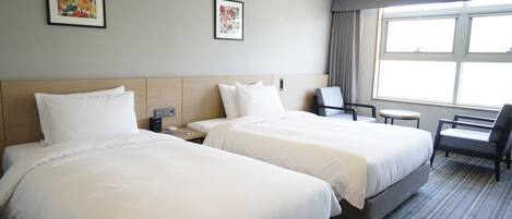 A hotel room with two beds, a desk, a chair, and a window.
