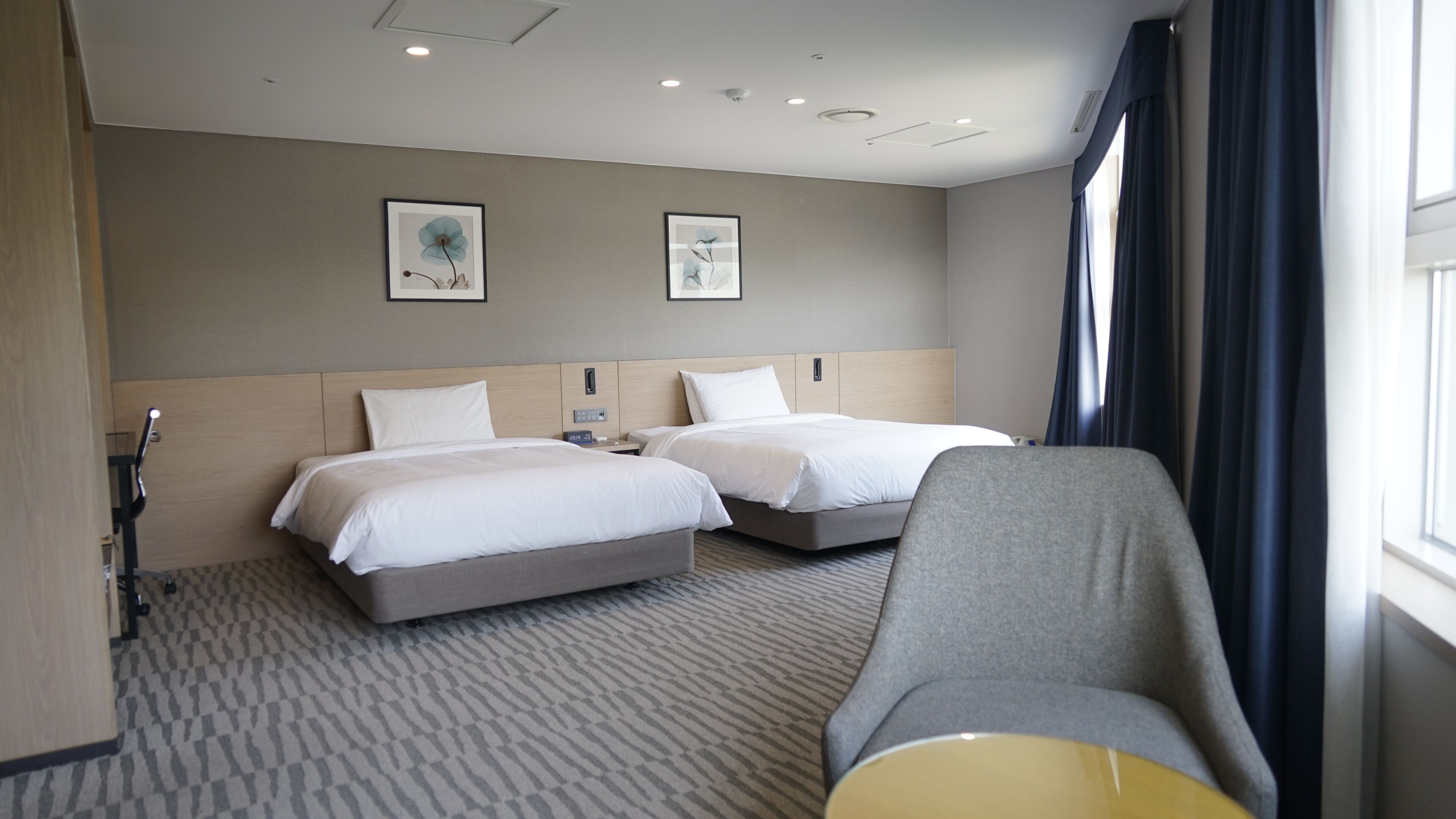 A hotel room with two beds, a sofa, a desk, and a window with curtains.