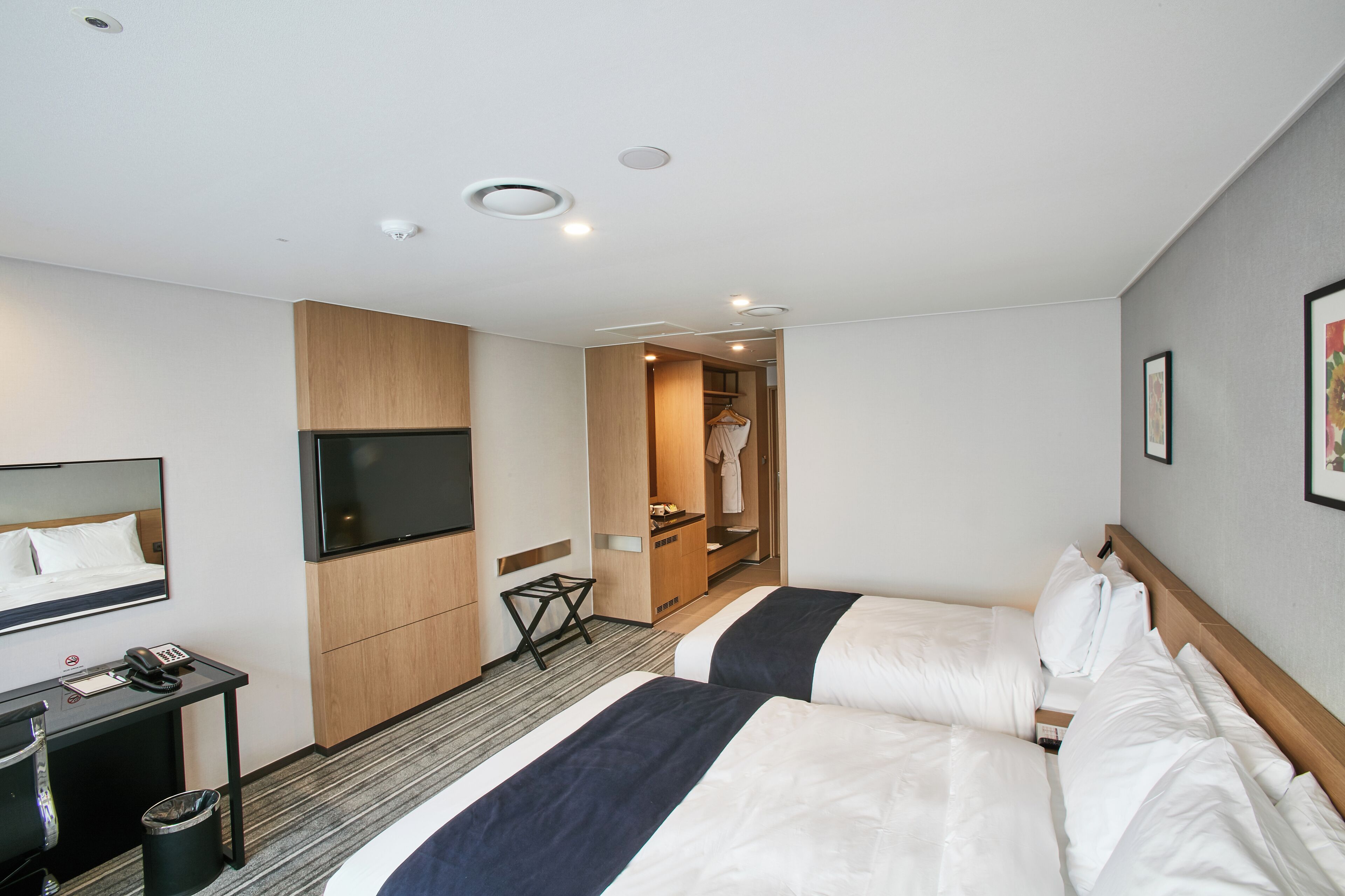 A hotel room with two beds, a TV, a desk with a phone, and a coat closet.