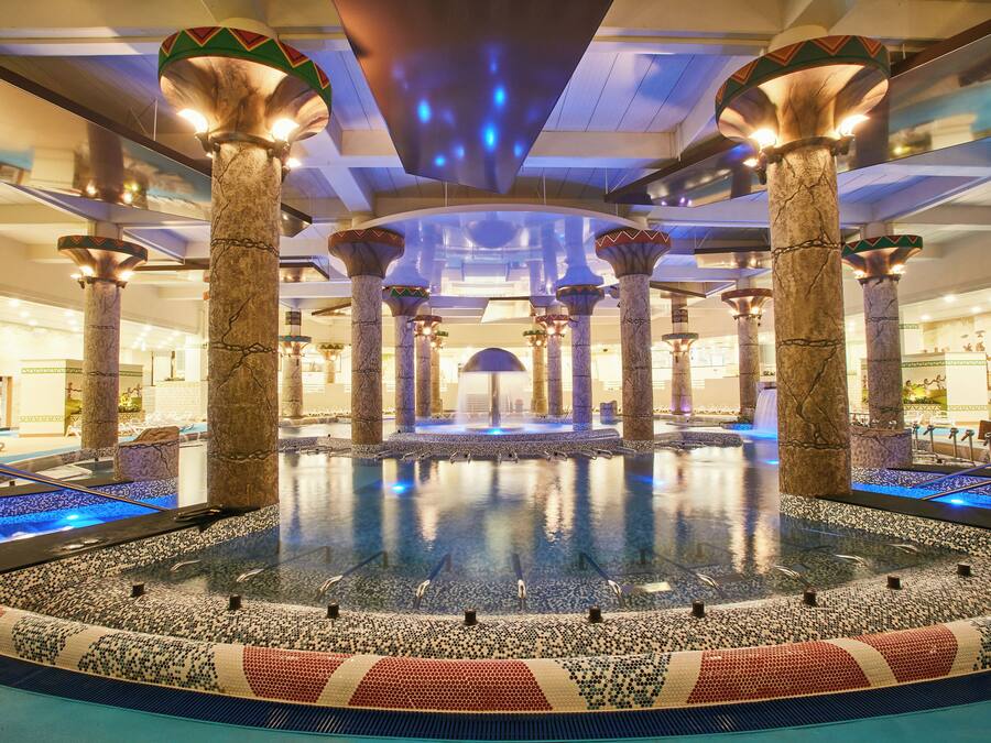 A luxurious indoor pool area with marble columns and a central water feature.