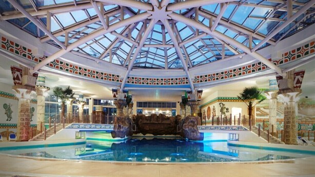 Una piscina interior con techo de cristal, rodeada de columnas ornamentales y detalles decorativos.