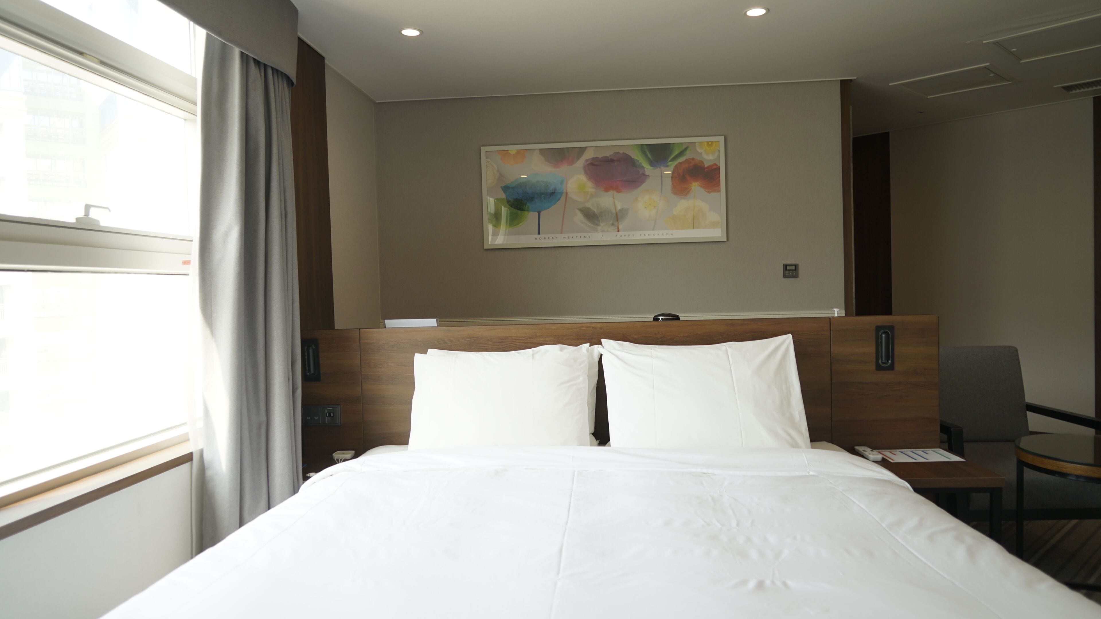 A hotel room with a bed, a painting on the wall, a chair, and a window with curtains.