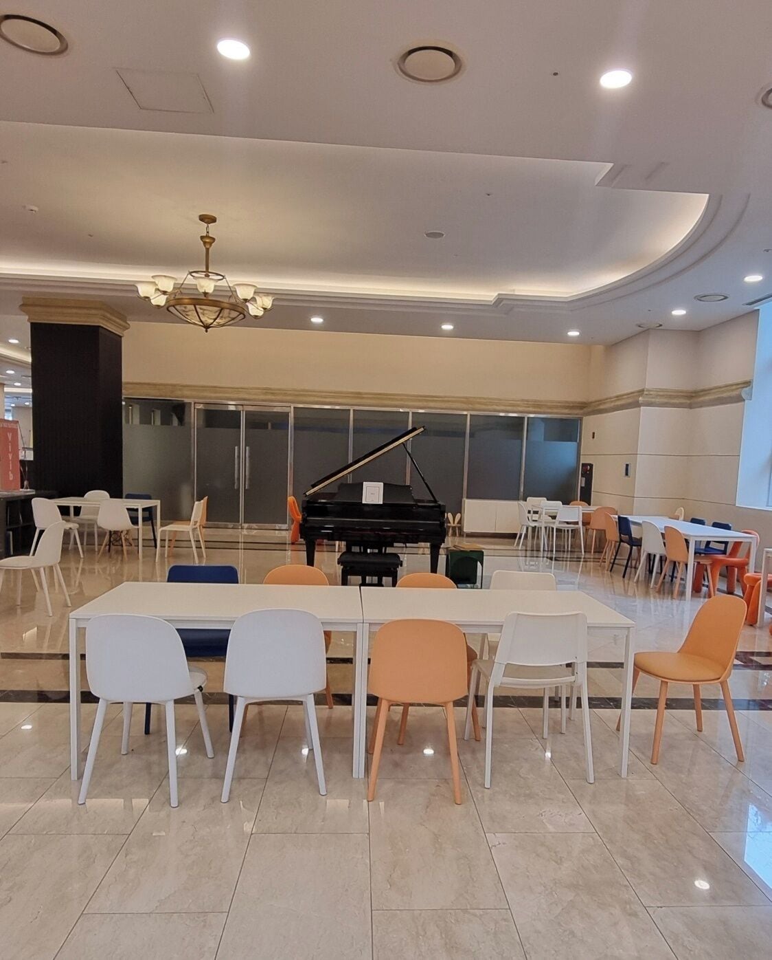 Une pièce spacieuse avec un grand piano, des chaises blanches et orange, et un lustre.