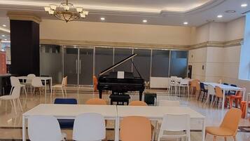 Un'ampia stanza con un pianoforte a coda, sedie bianche e arancioni e un lampadario.