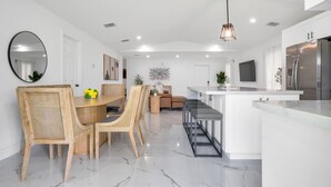 Une cuisine moderne avec des meubles blancs, un réfrigérateur en acier inoxydable et un coin repas comprenant une table et des chaises en bois.