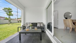 Un salon moderne comprenant un canapé, une table basse et des fauteuils, de grandes fenêtres et une porte-fenêtre coulissante donnant sur une terrasse.
