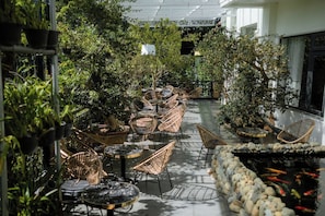 An indoor garden with wicker chairs and tables, surrounded by lush greenery and a koi pond. - A Quan Khoi Hotel DL - by Bay Luxury (Xuan Huong - Da Lat)