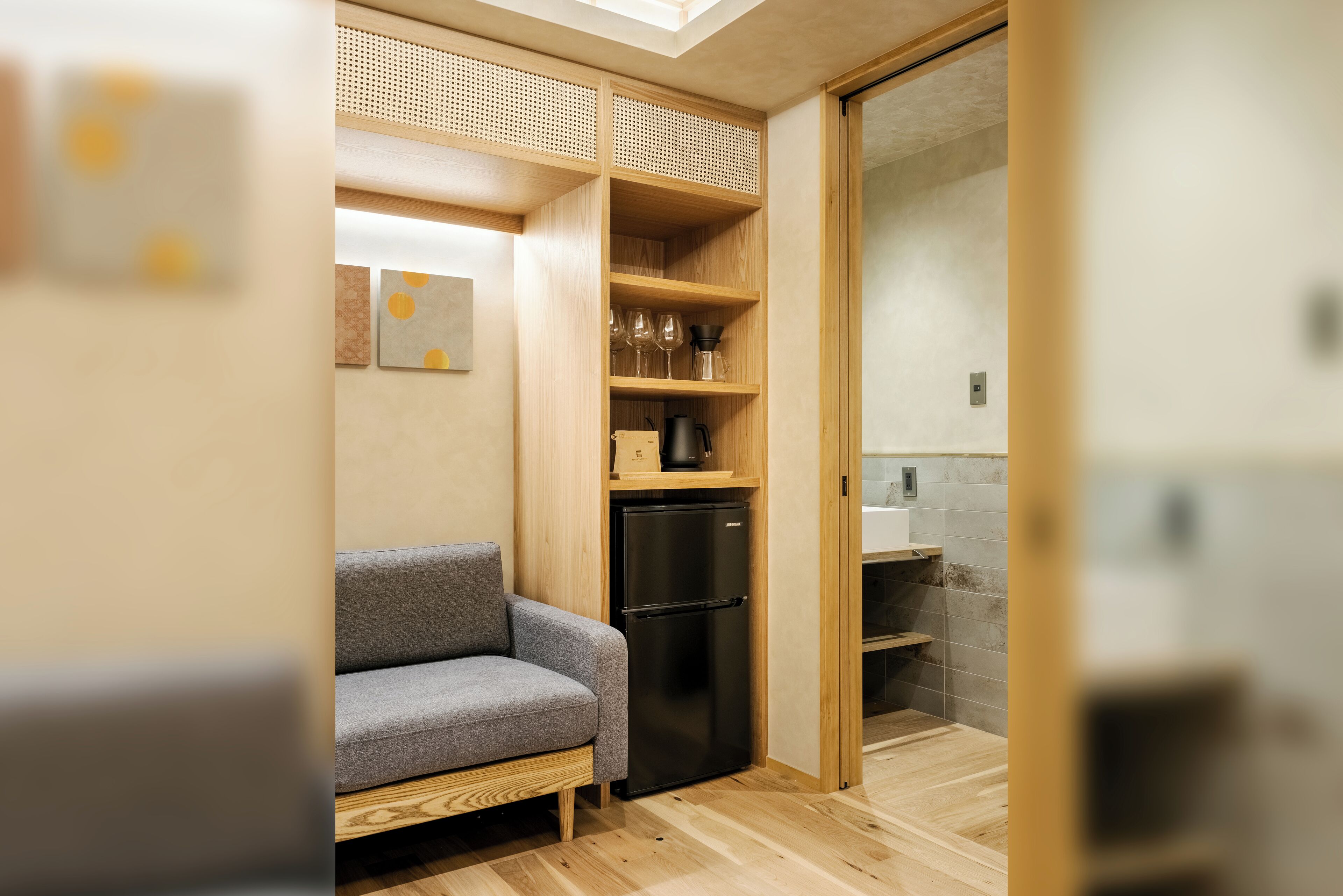 A compact kitchen with a built-in refrigerator, wooden shelves, and a grey sofa.