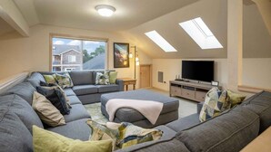 A spacious living room with a sectional sofa, a television, and skylights. - Wonderful North End Seaside Home, Fenced Backyard, Backyard Patio, 1 Mile to Shops, Food, and Fun (Seaside)