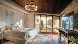 Ein Schlafzimmer mit einem großen Bett, einer Chandelier, einem Fernseher und Blick ins Freie.