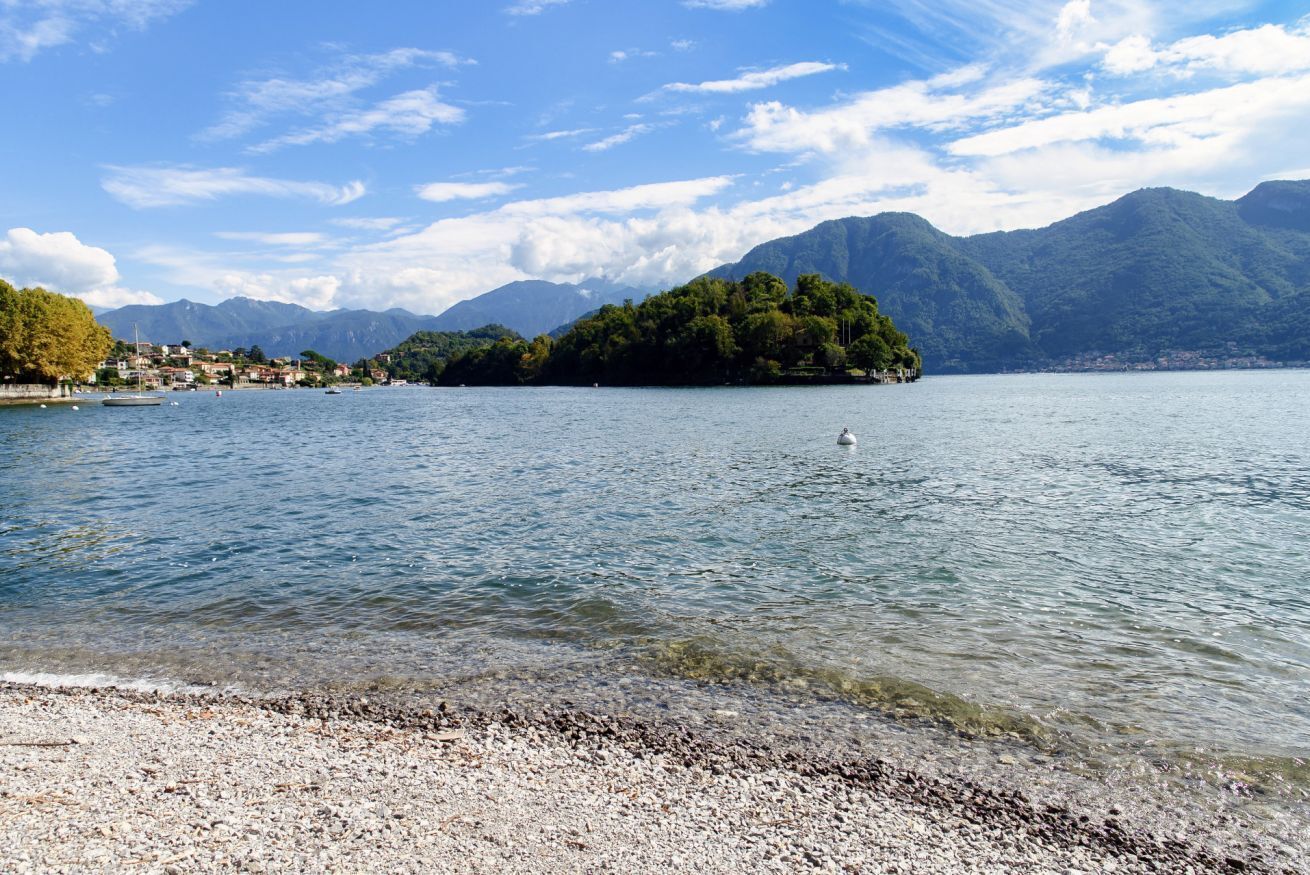 A lake with a small island, clear water, and mountains in the background.