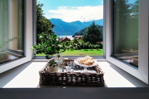 A wicker tray with pastries and a vase on a windowsill, overlooking a mountainous landscape.