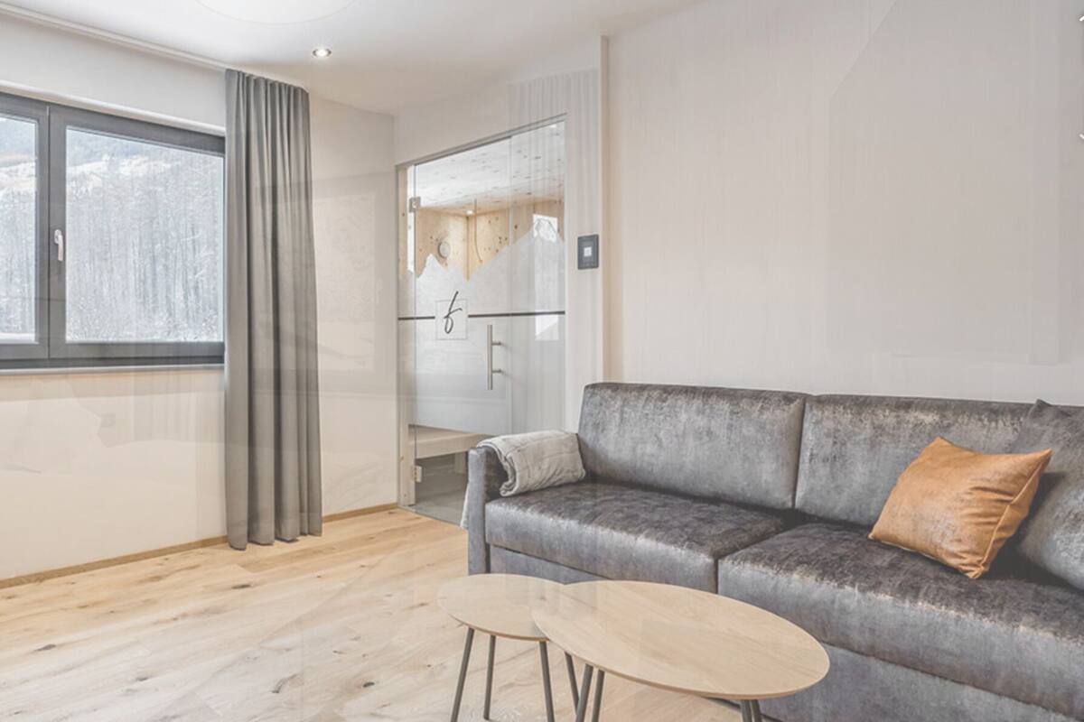 A modern living room with a grey sofa, a small round table, and a large window with curtains.