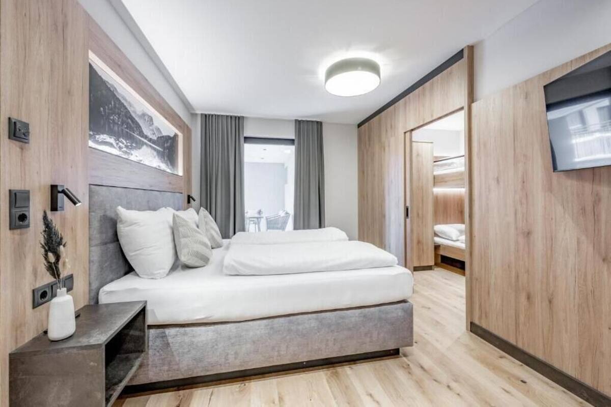 A modern bedroom with a large bed, wooden paneling, a flat-screen TV, and a view of the outdoors.
