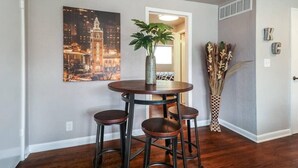 A dining area with a round table and four stools, a cityscape painting on the wall, and a plant in a vase. - First Floor with 2 King Bedrooms (Kansas City)
