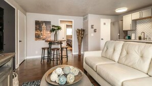 A modern living room with a sofa, a dining area with stools, and a kitchen with white cabinets. - First Floor with 2 King Bedrooms (Kansas City)