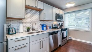 A modern kitchen with white cabinets, a stainless steel dishwasher, and a microwave. - First Floor with 2 King Bedrooms (Kansas City)