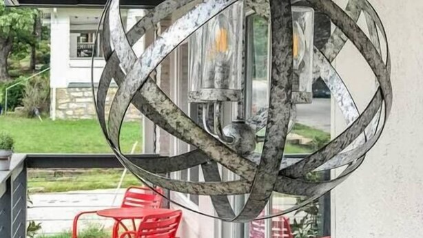 A spherical metal chandelier hanging from a ceiling, with a patio area featuring red chairs and a glass railing in the foreground. - First Floor with 2 King Bedrooms (Kansas City)