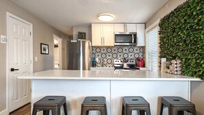 A modern kitchen with a central island, stainless steel appliances, and a decorative backsplash. - Cute Midtown 1 Bedroom (Kansas City)