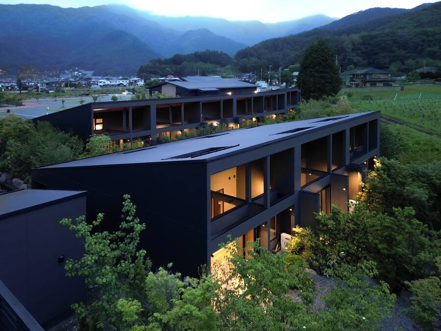 A modern building with multiple levels and large windows, surrounded by greenery and mountains in the background.