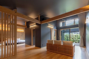 A modern hotel room with a wooden floor, a bed, a seating area with cushions, and large windows offering a view of the outdoors. - 7c villa & winery (Fujikawaguchiko)