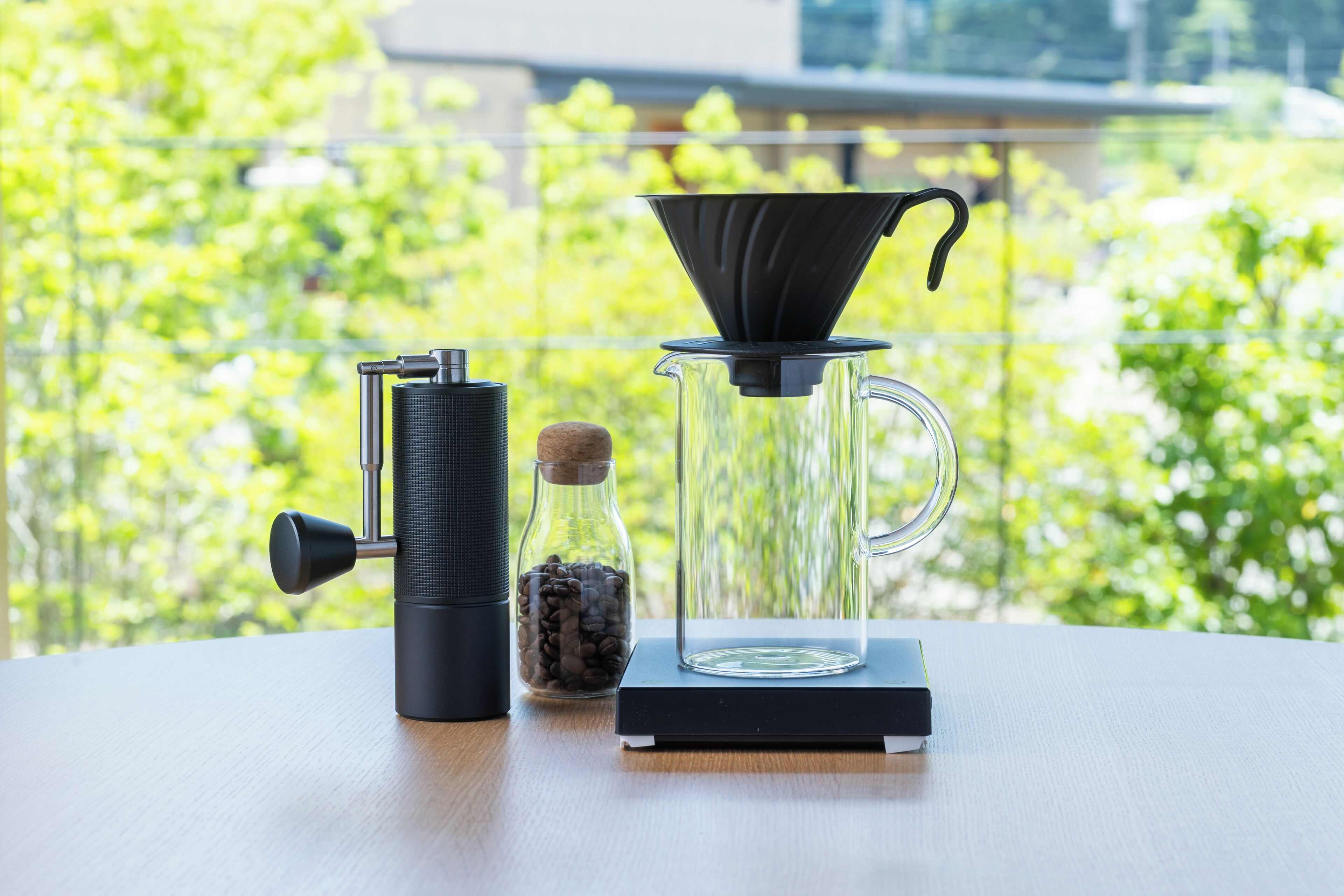 A coffee maker on a table with a clear glass pitcher and a container of coffee beans.