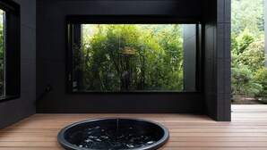 Un intérieur moderne avec un plancher en bois, une fontaine circulaire et une grande fenêtre donnant sur un jardin luxuriant.