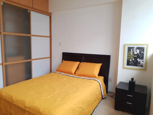Un dormitorio con cama, mesita de noche, una cita enmarcada en la pared y un armario con puertas de cristal.