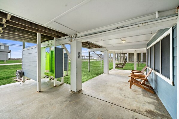 A covered outdoor area with a concrete floor, wooden chairs, and a green structure.