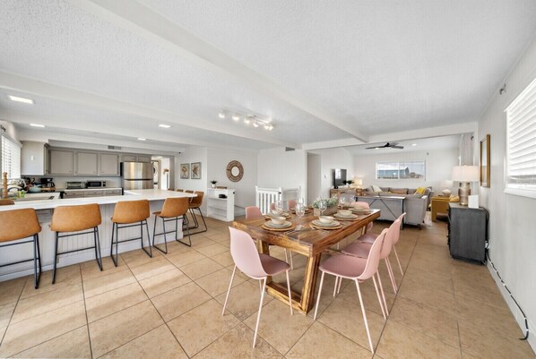 A spacious kitchen with a central island, dining area with pink chairs, and a large window.