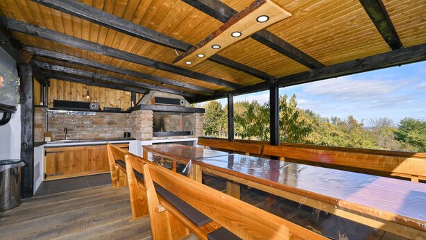 Una cocina al aire libre con horno de ladrillo, bancos de madera y vistas al bosque circundante.