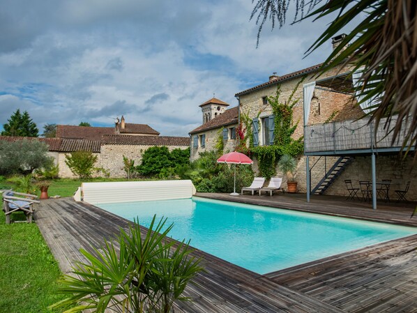 Relax by the serene pool surrounded by lush greenery and a rustic stone building.
