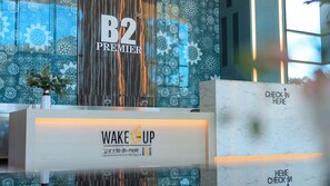 Un área de recepción con un letrero B2 Premier, una cafetería Wake Up y un mostrador de recepción.