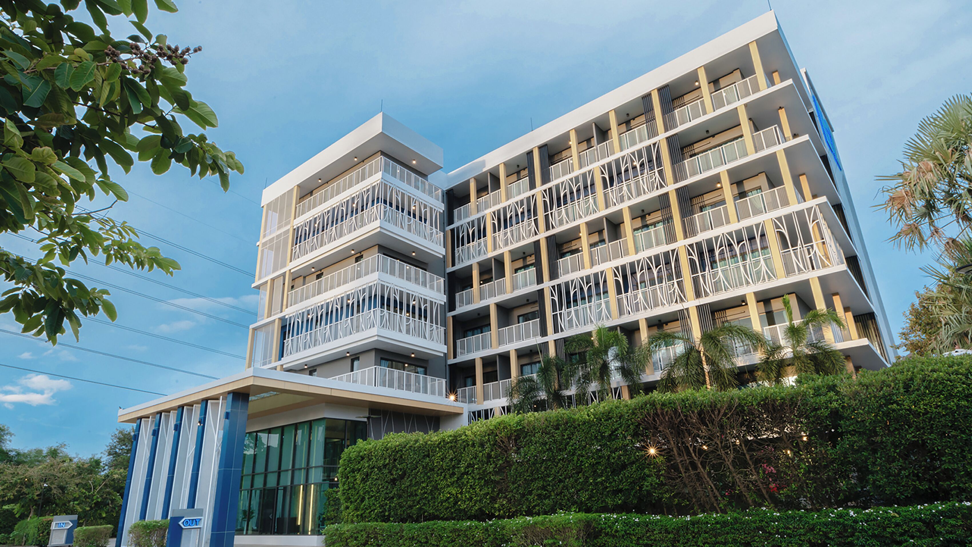 A multi-story hotel with balconies, a modern design, and a well-maintained garden area.