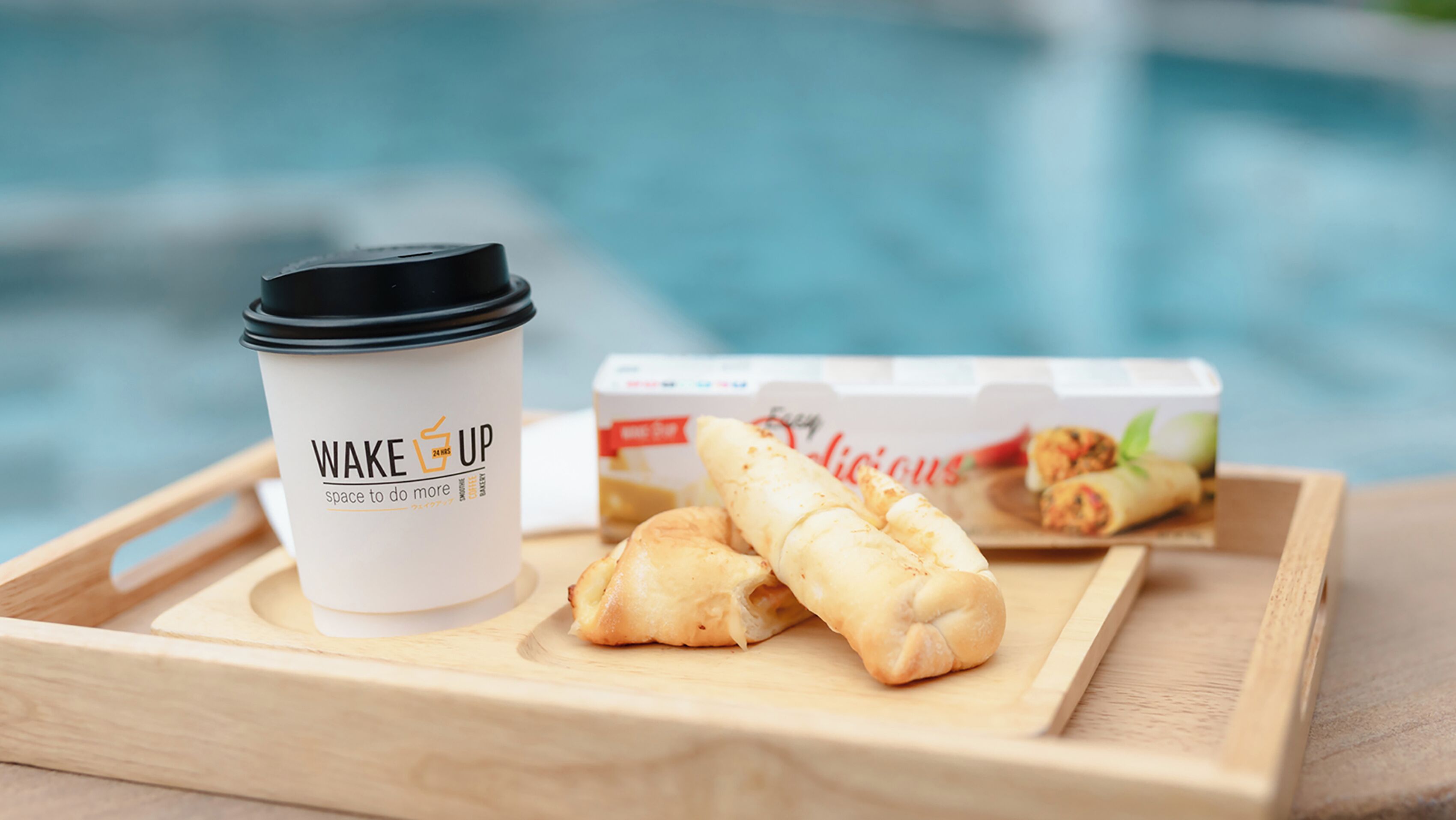 Una bandeja con una taza de café y rollitos primavera junto a una piscina.