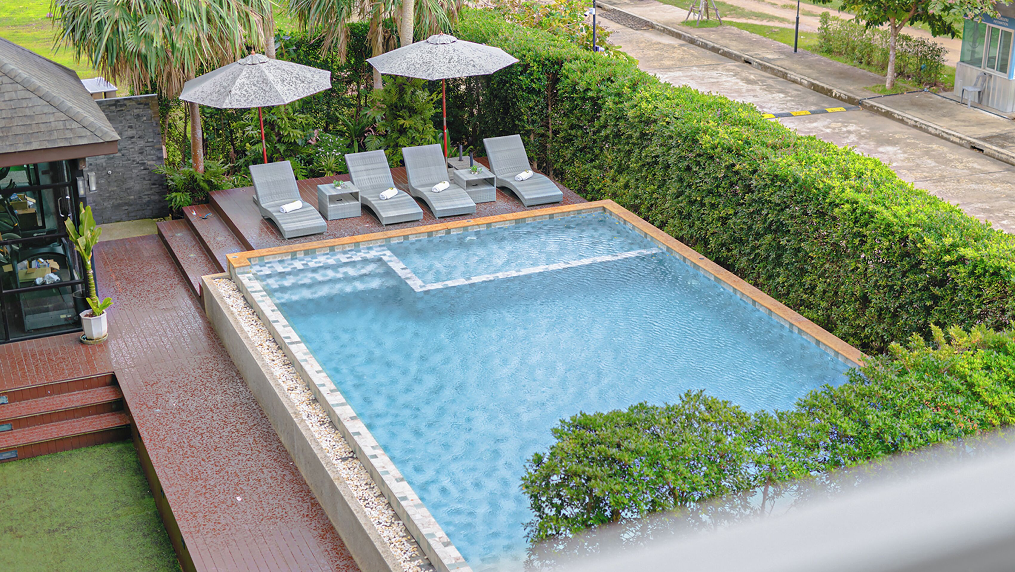 Piscina retangular com borda azulejada, cercada por um pequeno hedge, e equipada com espreguiçadeiras e guarda-sóis.