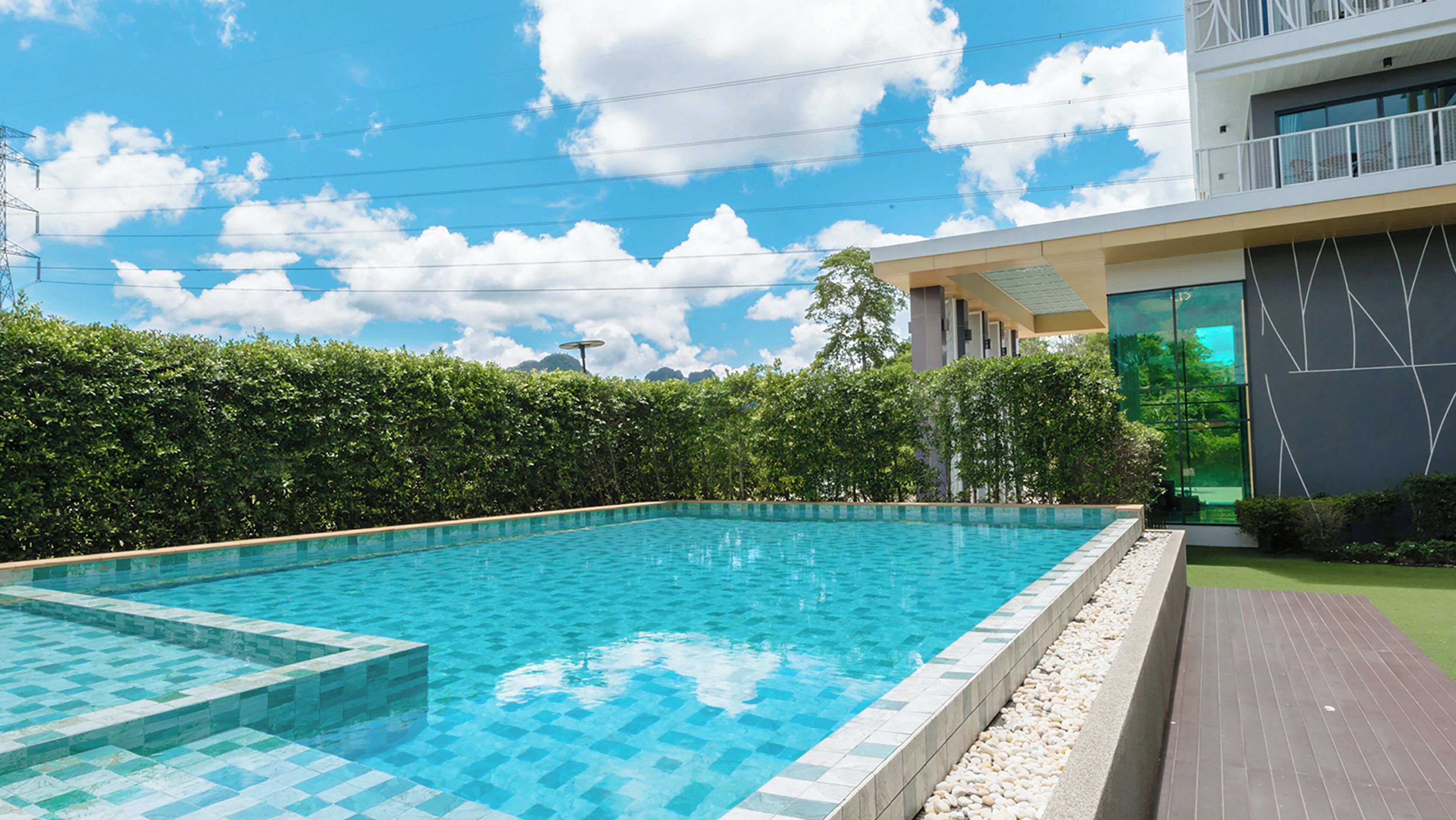 Ein rechteckiger Swimmingpool mit einer Fliesenbordsteinkante, umgeben von einer Hecke und einer Holzterrasse.