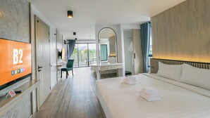 A hotel room with a large bed, a desk, a chair, a TV, and a balcony with a view.