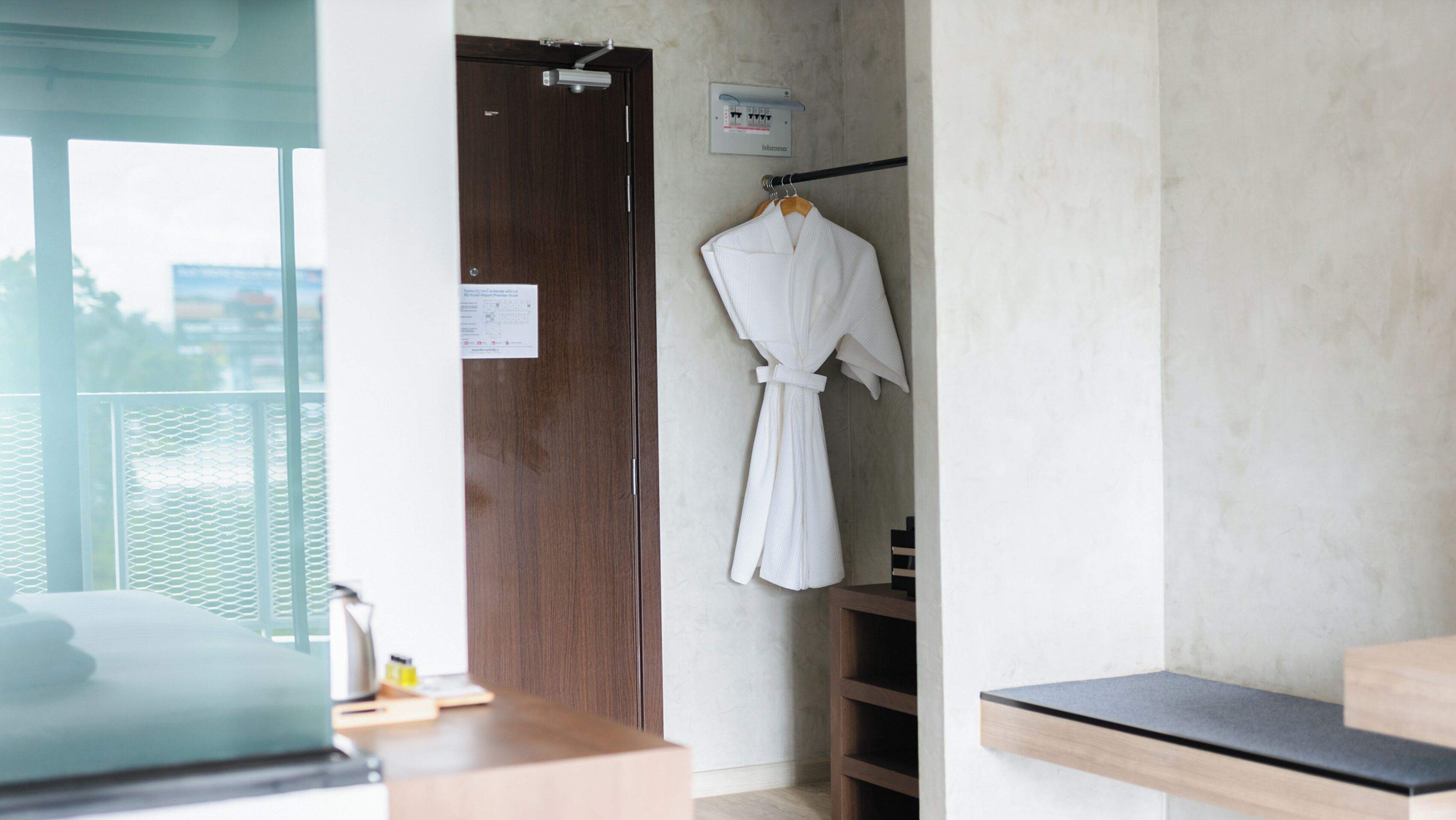 A hotel room with a wooden desk, a robe hanging on a rack, and a door with a sign.