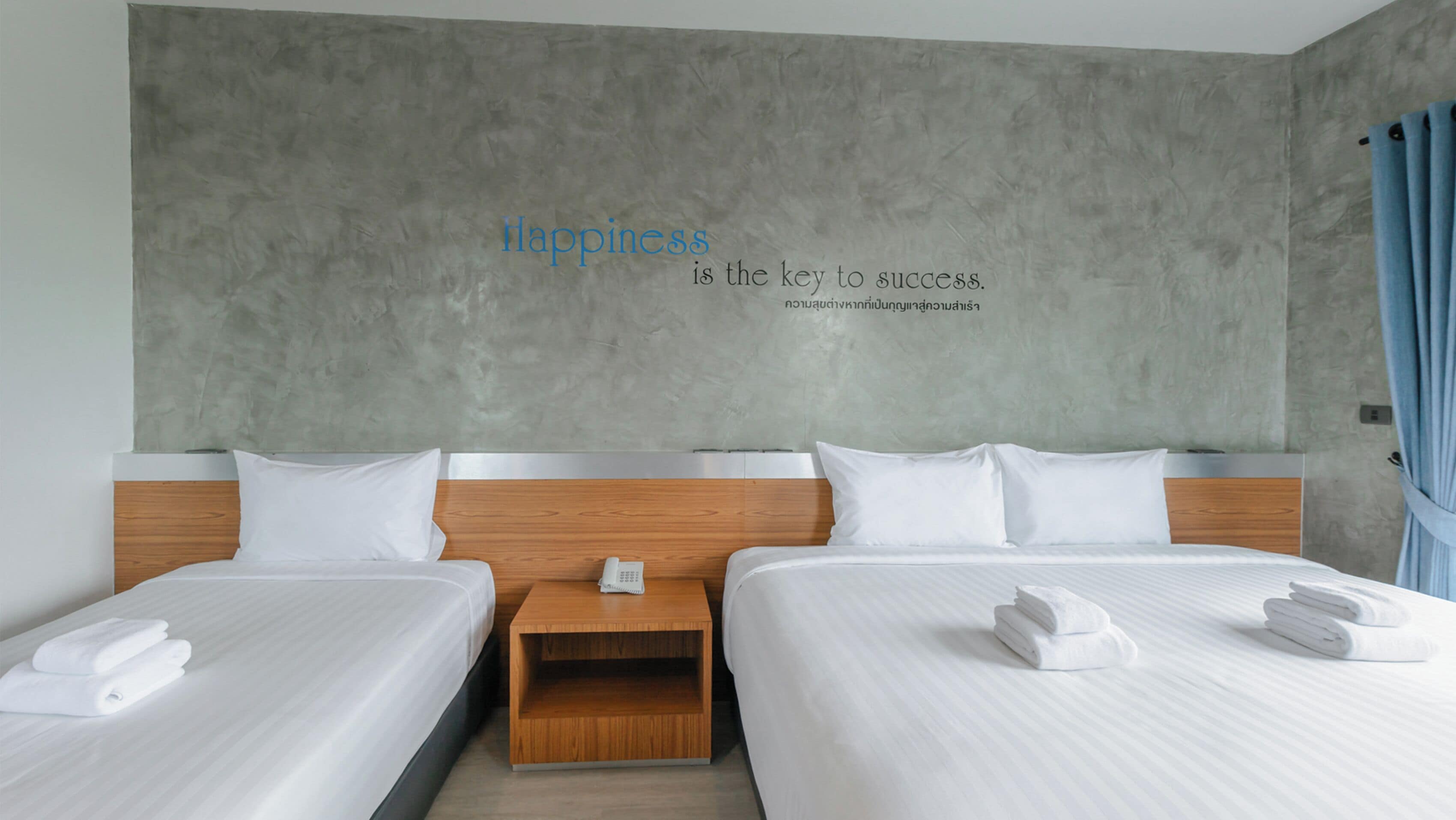 Ein Hotelzimmer mit zwei Betten, einem Nachttisch aus Holz und einer Wand mit einem motivierenden Zitat.