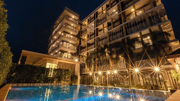 A multi-story hotel with a swimming pool, balconies, and outdoor lighting.