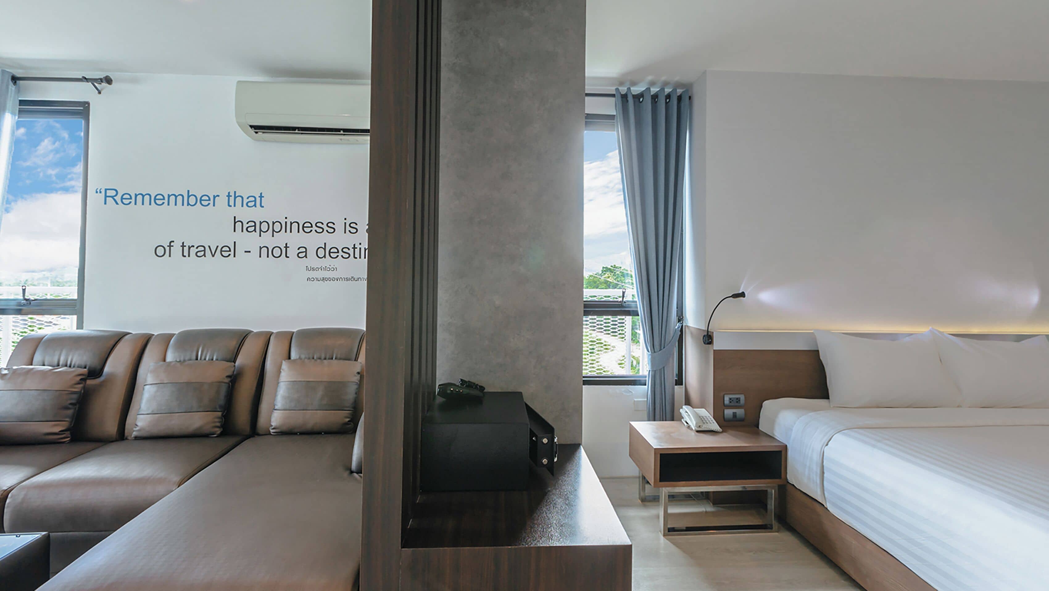 A modern hotel room with a sofa, a bed, a nightstand, and a wall with a motivational quote.