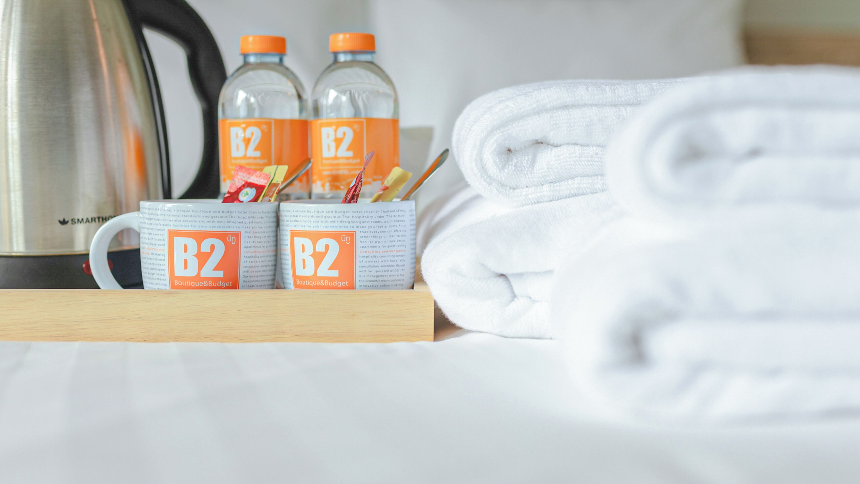 A neatly arranged hotel room with a folded white towel, two B2 Boutique & Budget branded bottles, and a kettle on the table.
