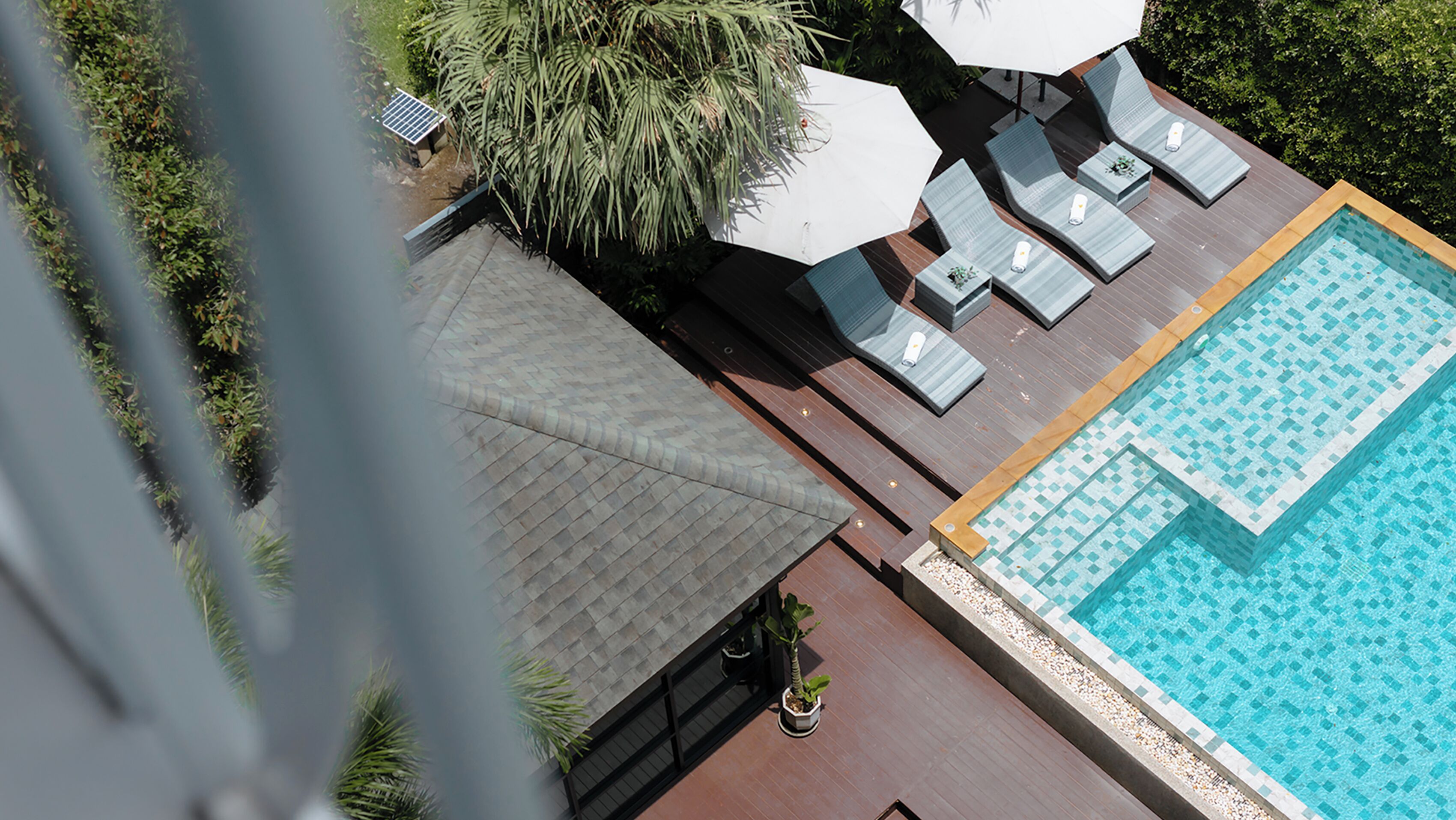 A rooftop pool area with lounge chairs and umbrellas, surrounded by greenery.