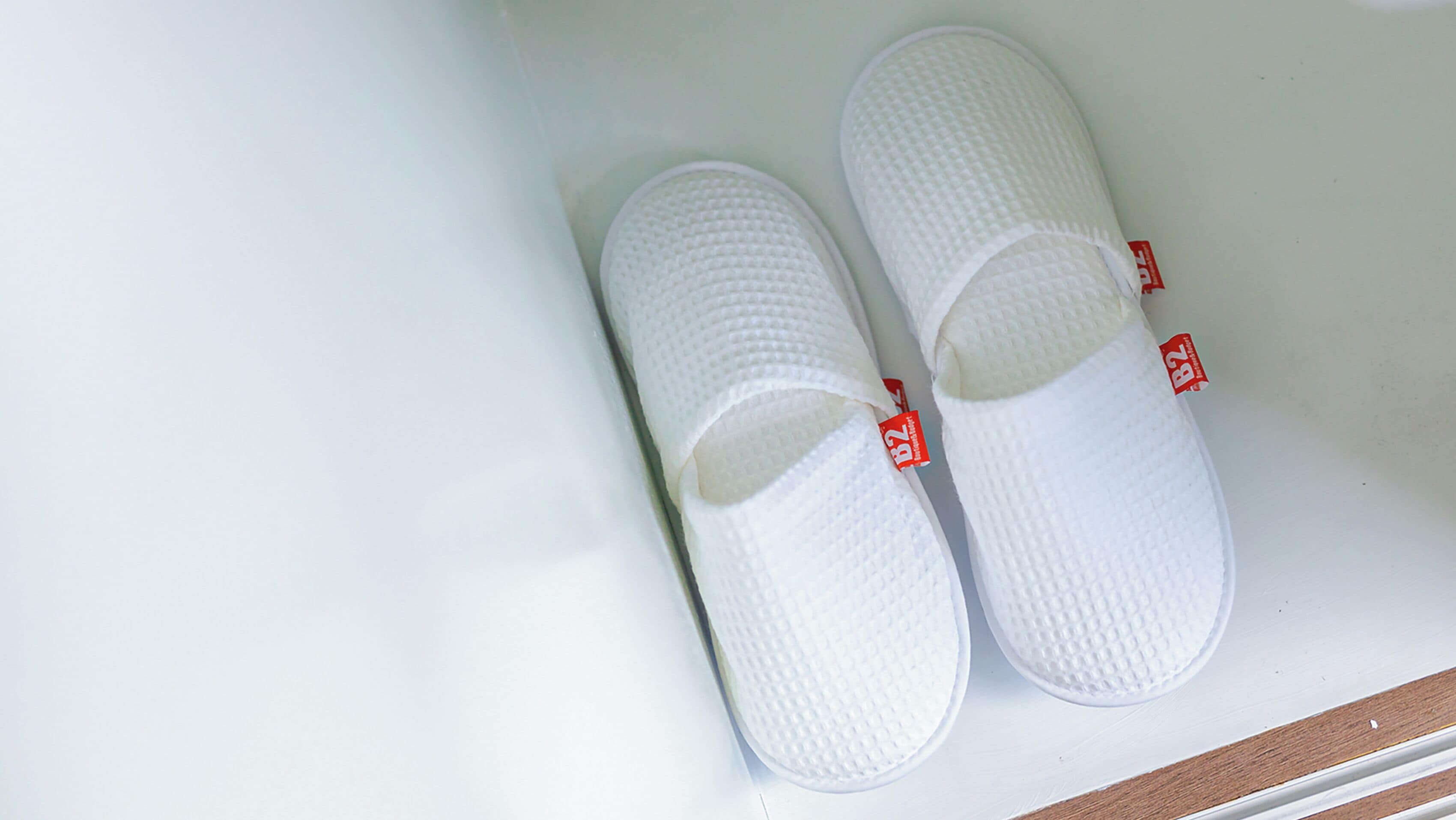 Un par de pantuflas blancas con etiquetas rojas sobre una superficie blanca.